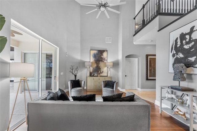 living room with a high ceiling, ceiling fan, and wood-type flooring