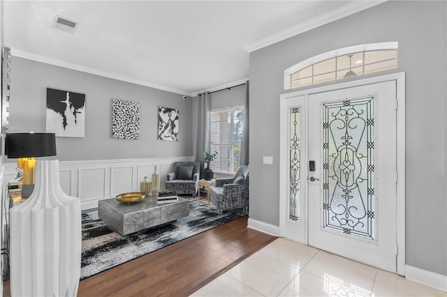 foyer featuring wood finished floors, a wainscoted wall, visible vents, crown molding, and a decorative wall