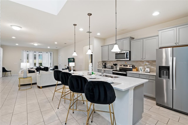 kitchen featuring appliances with stainless steel finishes, gray cabinetry, a kitchen island with sink, and a breakfast bar area