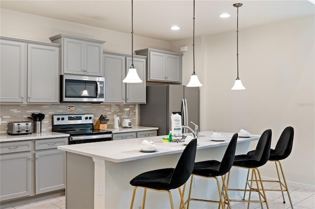 kitchen featuring backsplash, hanging light fixtures, stainless steel appliances, and a kitchen island with sink