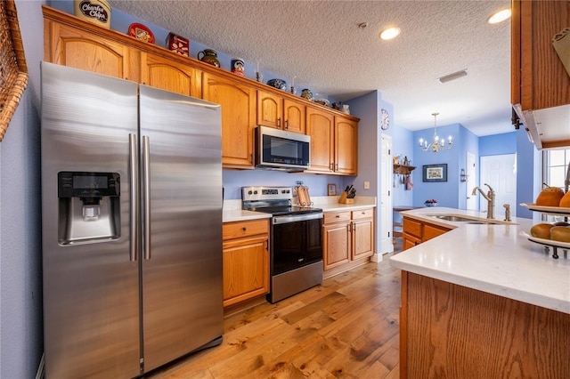 kitchen with pendant lighting, sink, light hardwood / wood-style flooring, an inviting chandelier, and stainless steel appliances