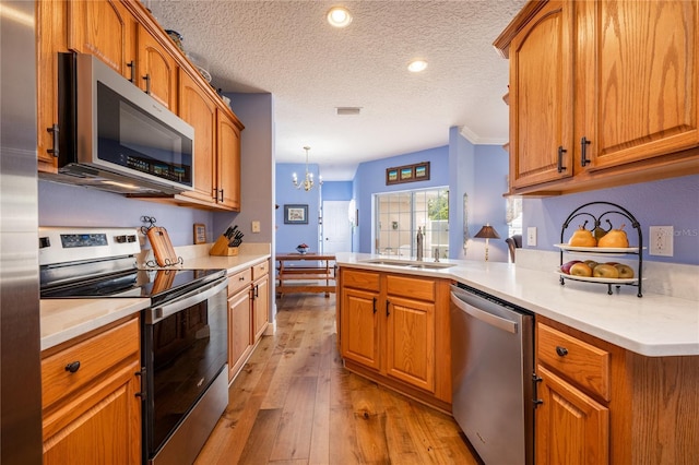 kitchen featuring sink, decorative light fixtures, a textured ceiling, light wood-type flooring, and appliances with stainless steel finishes