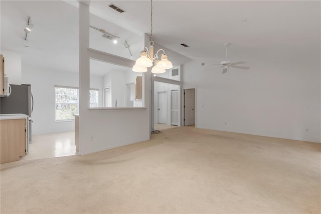 unfurnished living room with rail lighting, ceiling fan with notable chandelier, light colored carpet, and high vaulted ceiling