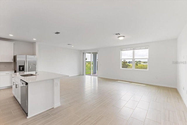 kitchen with stainless steel appliances, white cabinetry, sink, and an island with sink