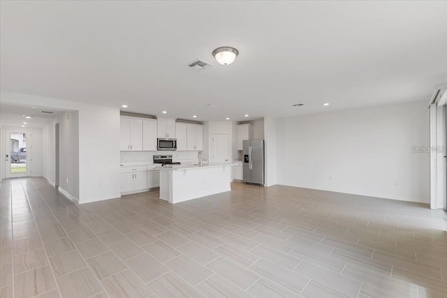 kitchen with a center island with sink, light tile patterned floors, white cabinetry, appliances with stainless steel finishes, and sink