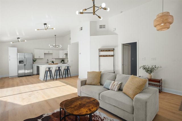 living room featuring high vaulted ceiling, a notable chandelier, and light hardwood / wood-style floors