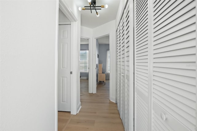 hallway with light wood-type flooring and an inviting chandelier