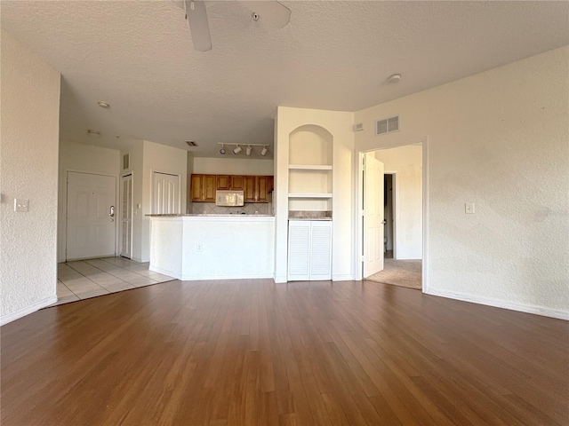 unfurnished living room featuring a textured ceiling, ceiling fan, light wood-type flooring, and built in features