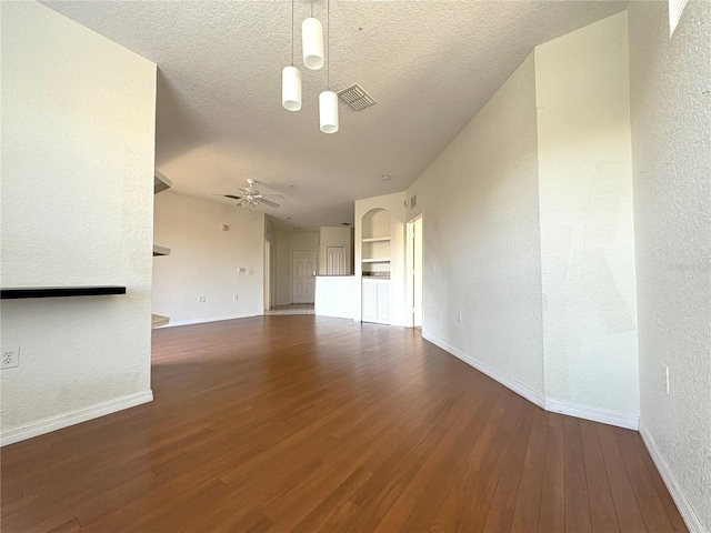 unfurnished living room with ceiling fan, dark wood-type flooring, built in shelves, and a textured ceiling