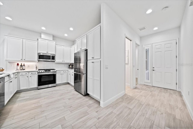 kitchen featuring appliances with stainless steel finishes, white cabinets, light wood-type flooring, and decorative backsplash