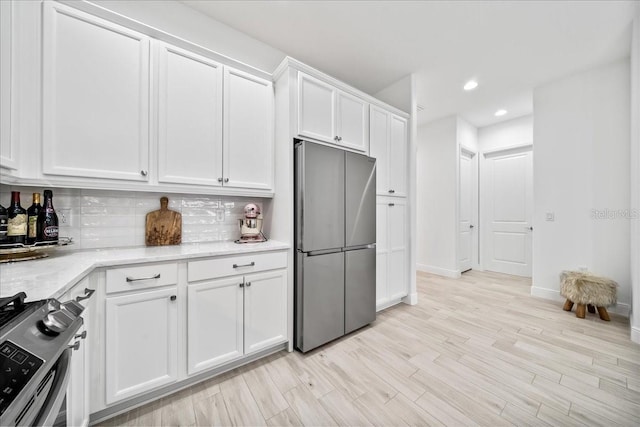 kitchen with stainless steel appliances, tasteful backsplash, white cabinets, and light hardwood / wood-style floors