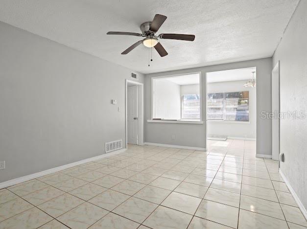 tiled empty room with ceiling fan and a textured ceiling