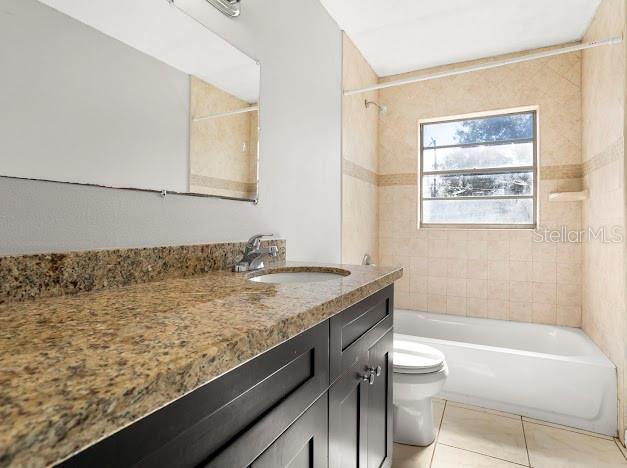 full bathroom with toilet, tiled shower / bath, tile patterned floors, and vanity