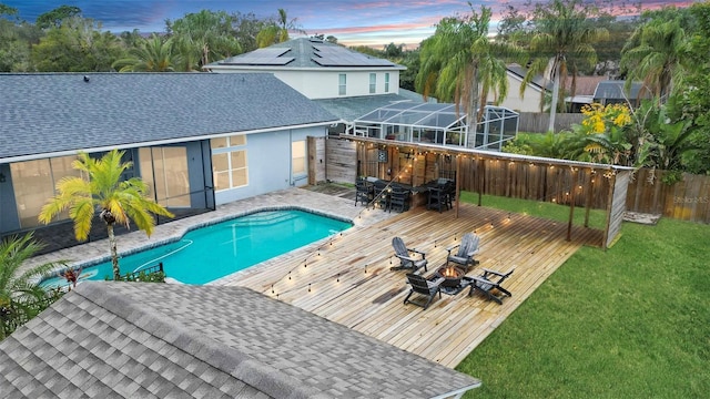 pool at dusk featuring a lawn, a deck, and glass enclosure