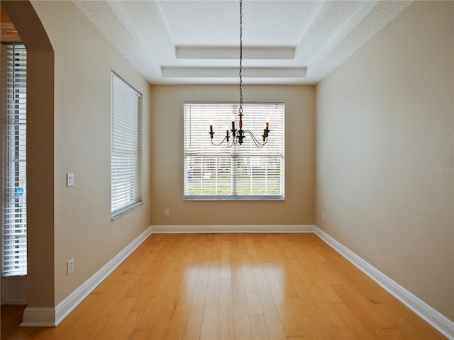 unfurnished dining area with light hardwood / wood-style floors, a textured ceiling, a raised ceiling, and an inviting chandelier