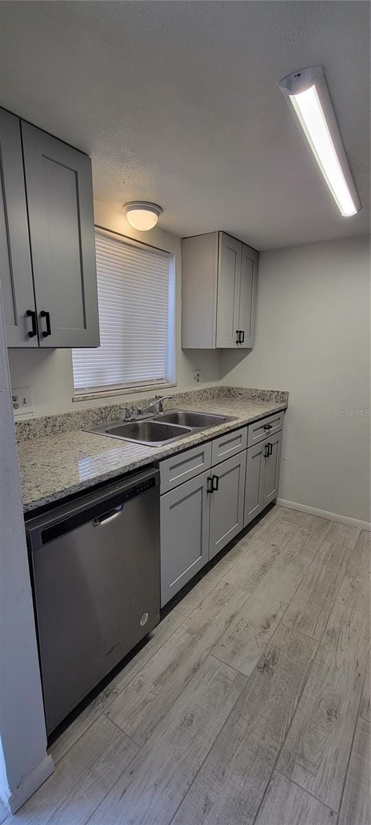 kitchen with light stone countertops, stainless steel dishwasher, light wood-type flooring, gray cabinetry, and sink