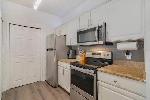 kitchen featuring appliances with stainless steel finishes, light stone countertops, white cabinets, decorative backsplash, and light wood-type flooring