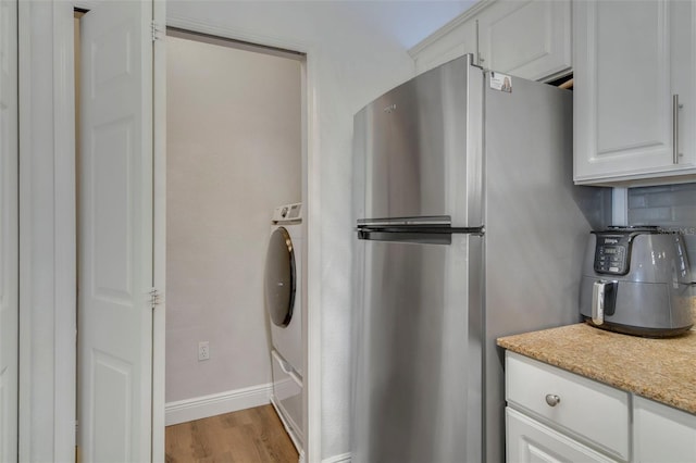 interior space featuring light hardwood / wood-style flooring, stainless steel refrigerator, light stone countertops, decorative backsplash, and white cabinets