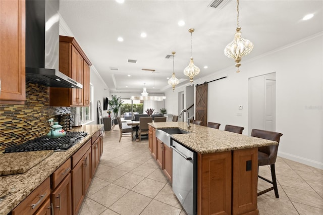 kitchen featuring wall chimney range hood, stainless steel appliances, a kitchen island with sink, a breakfast bar, and a barn door