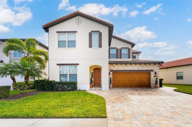 mediterranean / spanish-style house featuring a tile roof, stone siding, decorative driveway, stucco siding, and a front yard