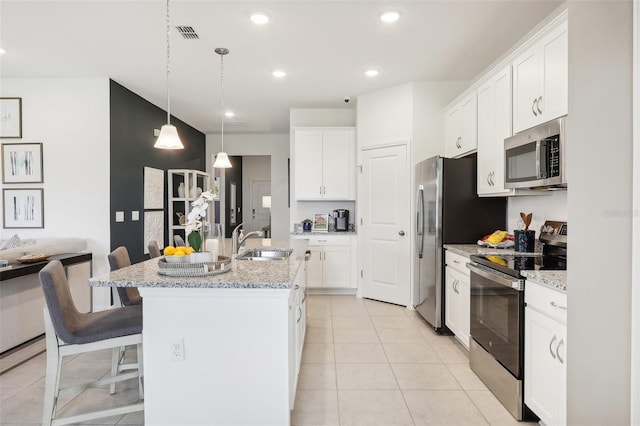 kitchen featuring white cabinets, a center island with sink, stainless steel appliances, light stone countertops, and sink