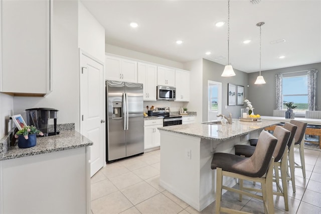 kitchen with a kitchen breakfast bar, white cabinetry, light stone counters, and appliances with stainless steel finishes