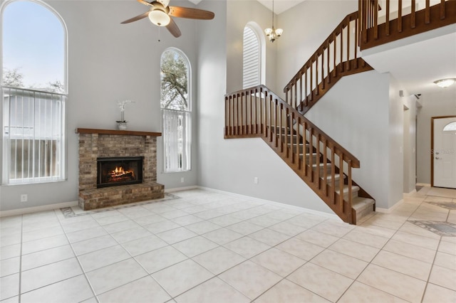 tiled living room featuring a brick fireplace, a towering ceiling, and ceiling fan