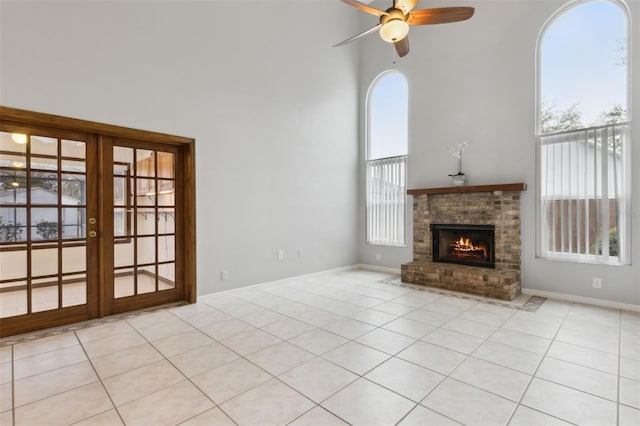 unfurnished living room with french doors, a brick fireplace, light tile patterned floors, a towering ceiling, and ceiling fan