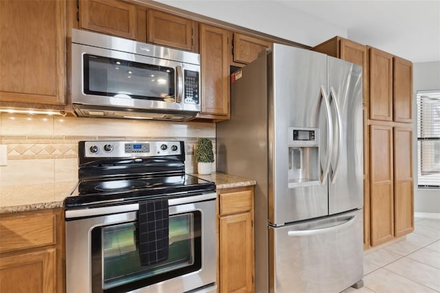 kitchen featuring stainless steel appliances, light tile patterned flooring, light stone countertops, and decorative backsplash