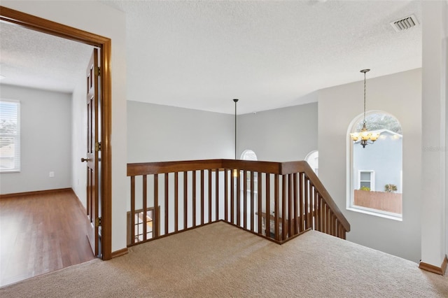 corridor with an inviting chandelier, plenty of natural light, a textured ceiling, and carpet