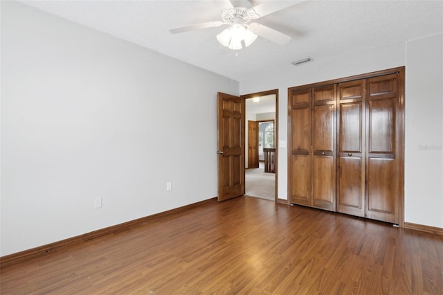 unfurnished bedroom featuring a textured ceiling, wood-type flooring, a closet, and ceiling fan