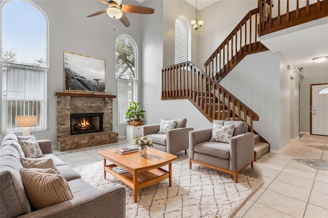 tiled living room featuring a fireplace, ceiling fan with notable chandelier, and a high ceiling