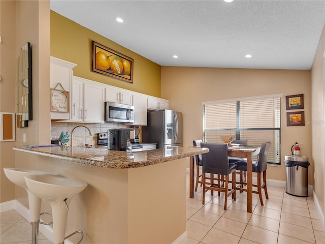 kitchen featuring appliances with stainless steel finishes, a kitchen bar, kitchen peninsula, and light tile patterned floors