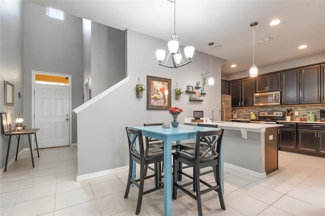 kitchen with a breakfast bar area, appliances with stainless steel finishes, hanging light fixtures, an island with sink, and dark brown cabinetry