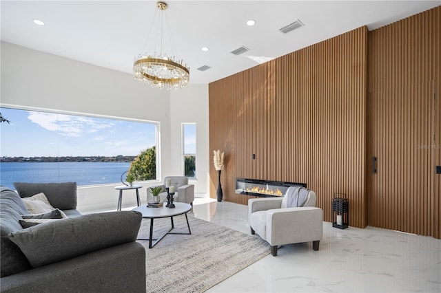 living room with a water view, a large fireplace, a chandelier, and wood walls