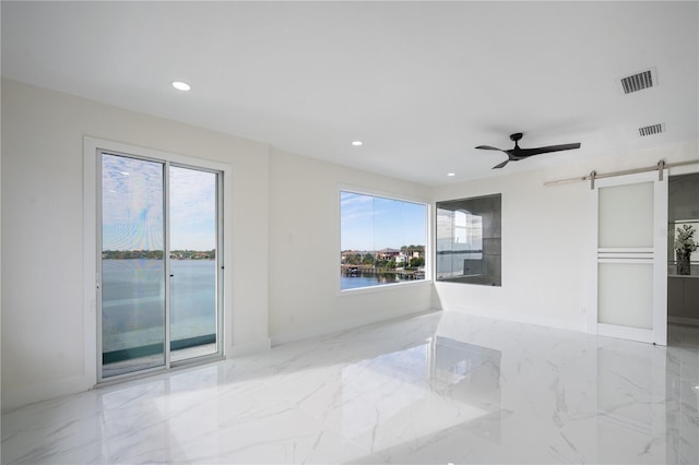 unfurnished room with a wealth of natural light, a barn door, ceiling fan, and a water view