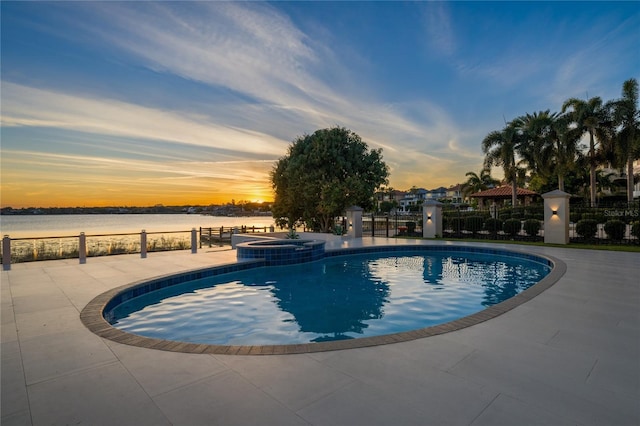 pool at dusk featuring a water view, an in ground hot tub, and a patio area