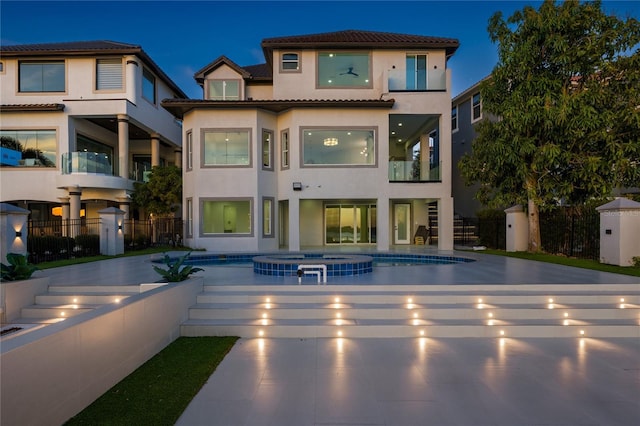 back house at night with a swimming pool with hot tub and a patio