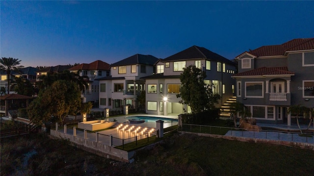 back house at dusk with a swimming pool with hot tub and a patio