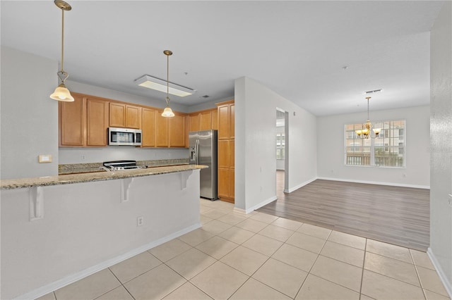 kitchen featuring stainless steel appliances, a kitchen breakfast bar, light tile patterned floors, kitchen peninsula, and a chandelier