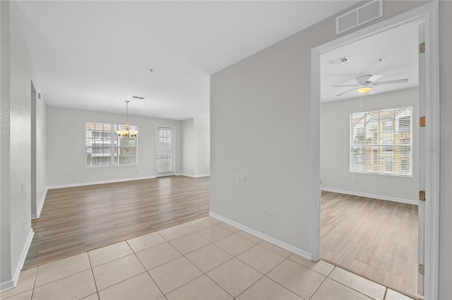 empty room with light tile patterned flooring and ceiling fan with notable chandelier