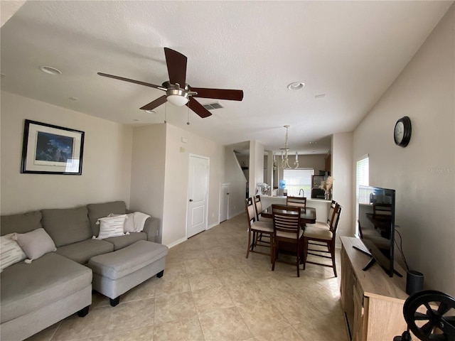 tiled living room featuring ceiling fan with notable chandelier and a textured ceiling