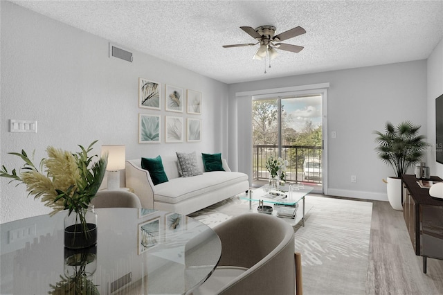 living room featuring ceiling fan, light hardwood / wood-style flooring, and a textured ceiling