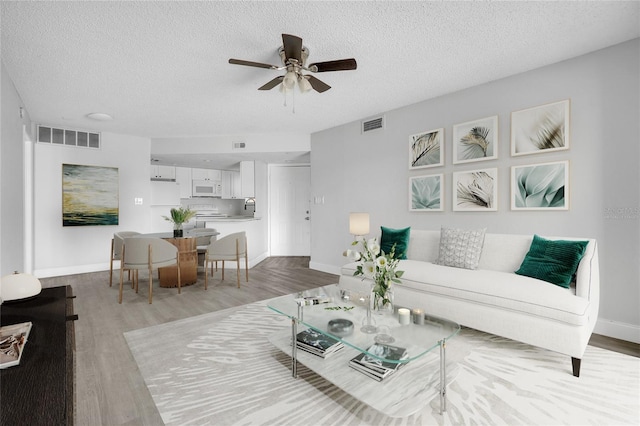 living room with ceiling fan, a textured ceiling, and light hardwood / wood-style floors