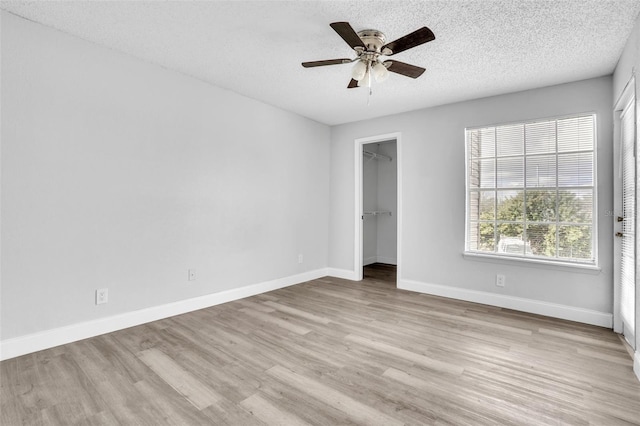 unfurnished bedroom with a spacious closet, a textured ceiling, a closet, ceiling fan, and light hardwood / wood-style floors