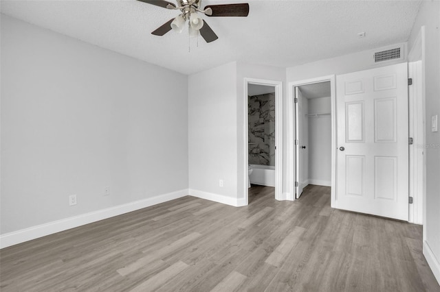 unfurnished bedroom with light hardwood / wood-style flooring, ceiling fan, a textured ceiling, a spacious closet, and a closet