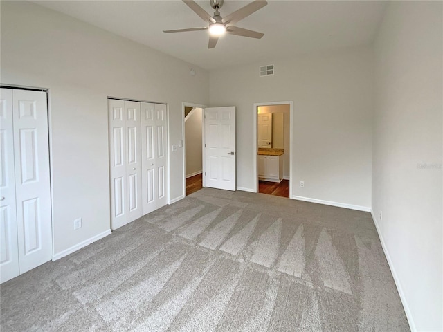 unfurnished bedroom featuring ensuite bathroom, ceiling fan, dark carpet, and multiple closets