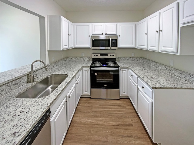 kitchen featuring appliances with stainless steel finishes, light wood-type flooring, light stone countertops, sink, and white cabinetry