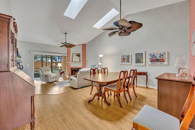 dining space with ceiling fan, a skylight, a fireplace, and light wood-type flooring