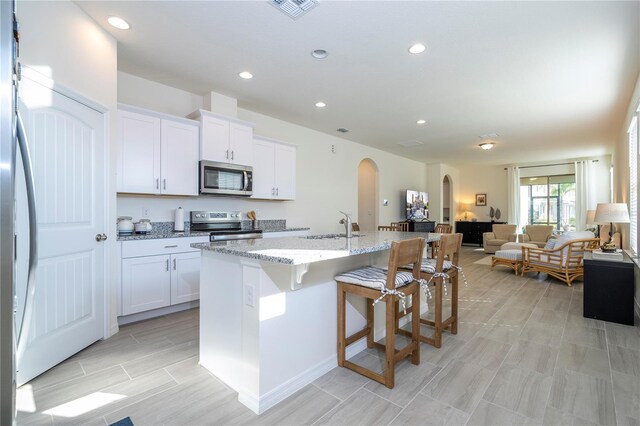 kitchen featuring stainless steel appliances, sink, white cabinets, light stone countertops, and a center island with sink